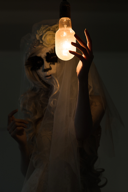 halloween witch. beautiful woman wearing s산타무에르테무에르테 mask casting spell near light bulb