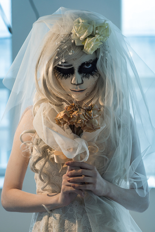 halloween witch. beautiful bride woman wearing s산타무에르테무에르테 mask and wedding dress holding dead bouquet of roses