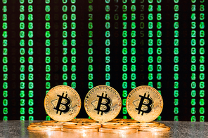 three bitcoins with sequence of green numbers in background