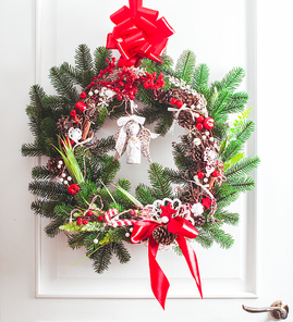 Christmas wreath hangs on the white doors. Red and white elements, bow for decorating holiday house