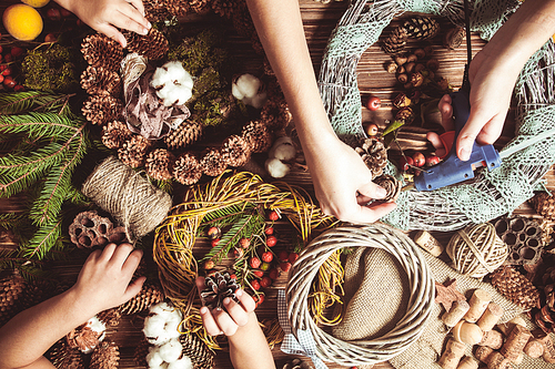 Mom with children making natural Christmas wreathes for decorate home. Top view table with hands