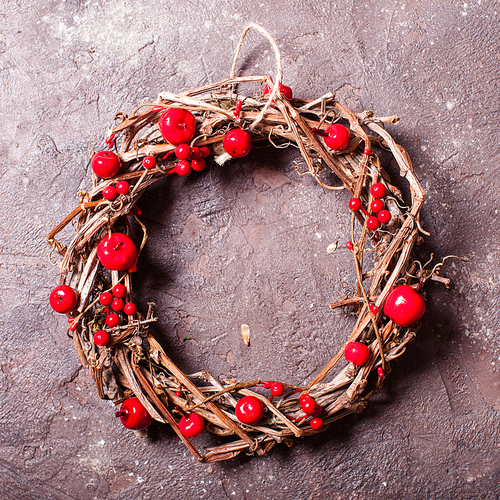 Woven wine wreath with red apples and berries over brown slate background. Holiday eco design