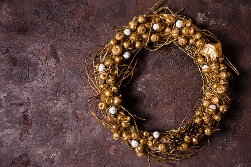 Golden woven natural wreath with acorns and pine cones on the brown marble wall