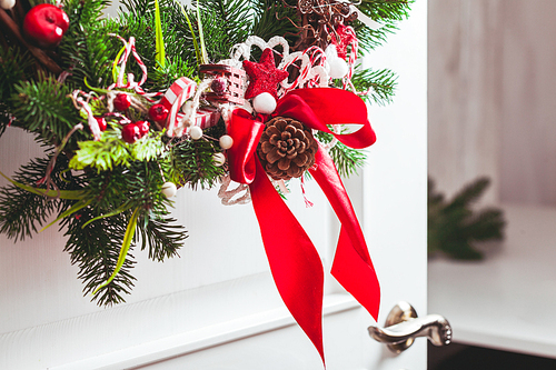Christmas wreath hangs on the white doors. Red and white elements, bow for decorating holiday house