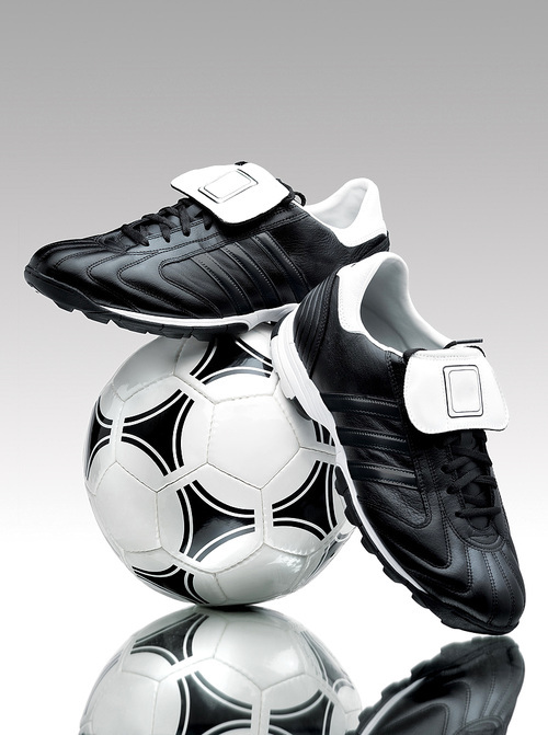 A pair of cool football boots standing on a ball on a reflective surface.
