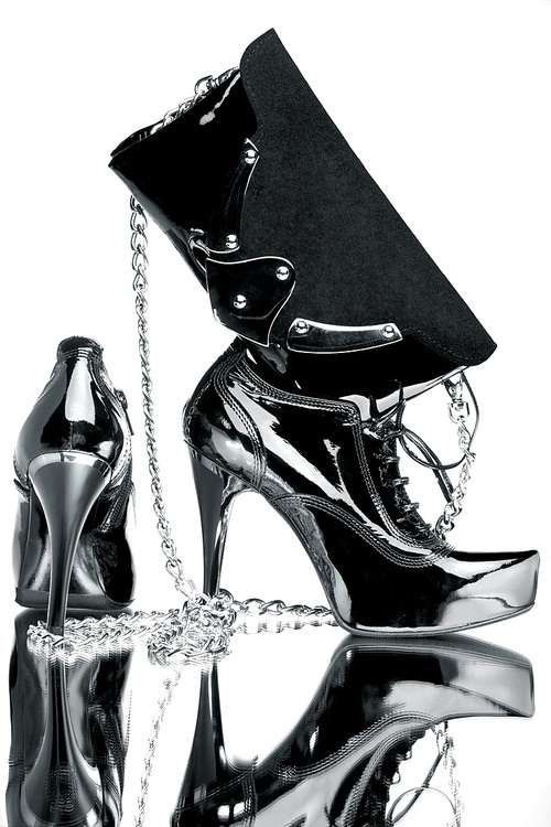 A close-up of a silver pair of shoes along with a stylish purse on a reflective surface.