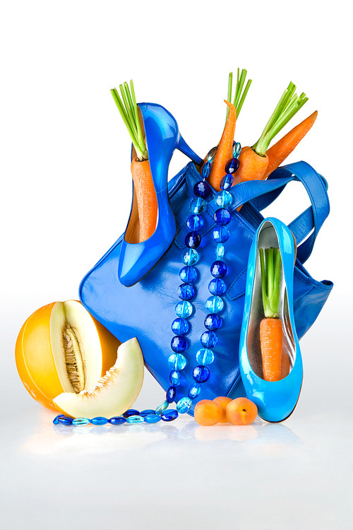 a still life of blue accessories, shoes, purse and necklace with carrots and