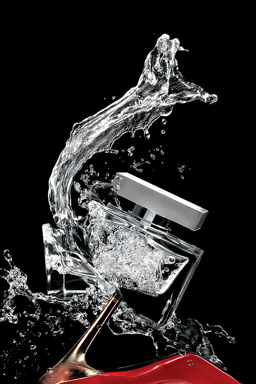 A transparent square glass bottle of perfume crashed with a metal heel.