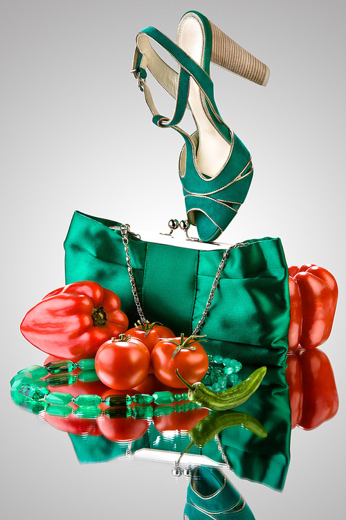 A close-up of a blue purse, high-heeled shoe, beads and vegetables.
