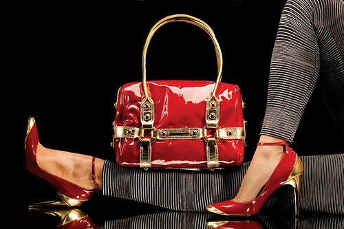 a close-up of a chic red handbag along with  female legs wearing elegant red shoes.