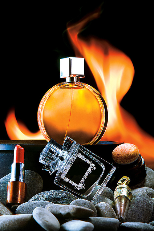A close-up of two bottles of male and female perfume and cosmetics against a flaming background.