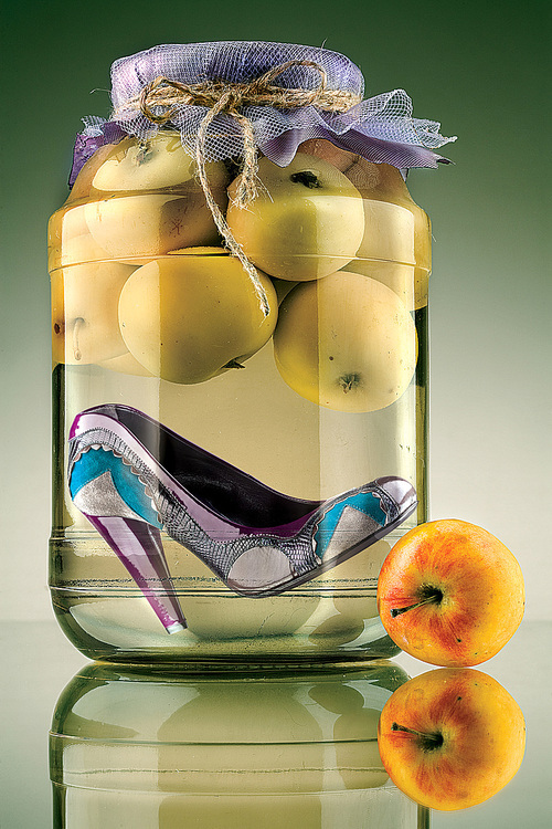 A close-up of a fashionable high-heeled shoe preserved in a glass jar with apples.