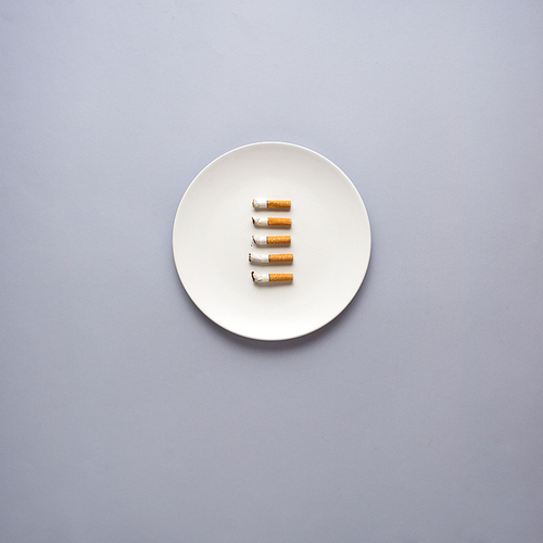 Creative concept photo of kitchenware with hand, painted plate with cigarettes on it on grey background.