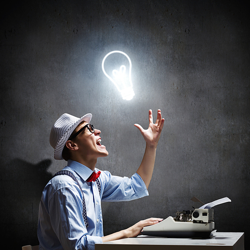 Young funny man in glasses writing on typewriter