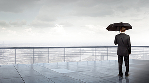 Back view of businessman with umbrella looking at city