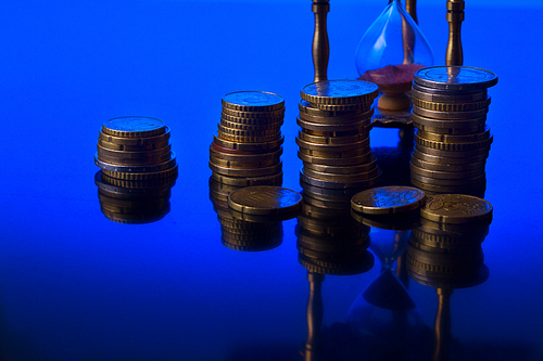 Time is money concept - hourglass with euro coins on blue background