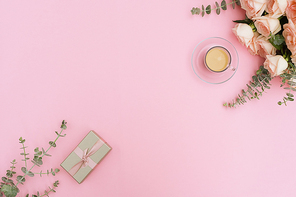 Cup of coffee with gift or present box and flowers on pink table from above, flat lay frame