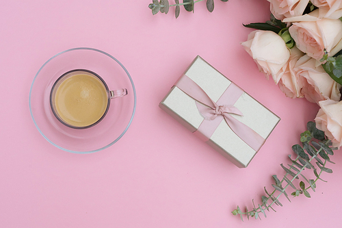 Morning cup of coffee with gift or present box and rose flowers on pink table from above, flat lay scene