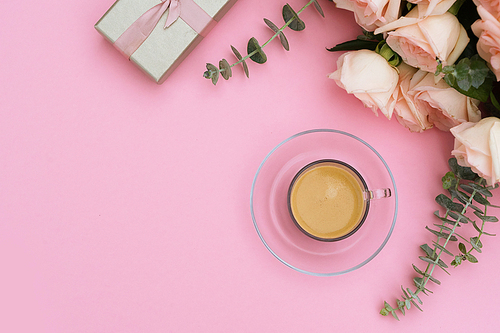 Morning cup of coffee with gift or present box and flowers on pink table from above, flat lay scene