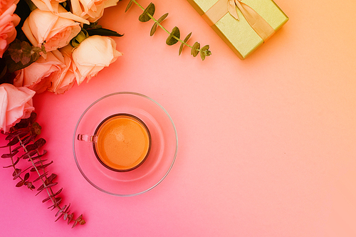 Morning cup of coffee with gift or present box and flowers on pink table from above, flat lay scene, toned