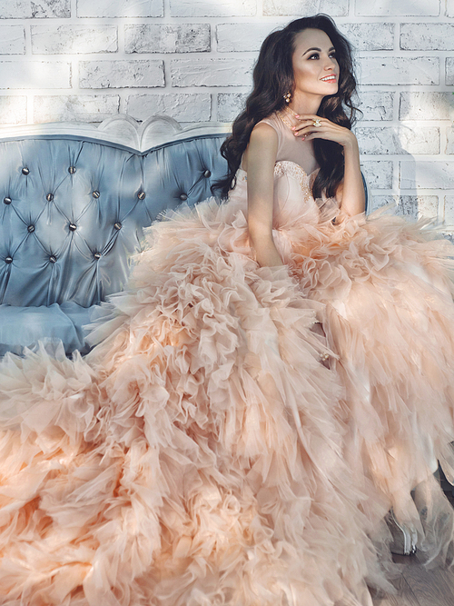 Fashionable portrait of beautiful lady in gorgeous couture dress on sofa. Holidays & Events. Evening dress. Princess dress. Christmas and New Year