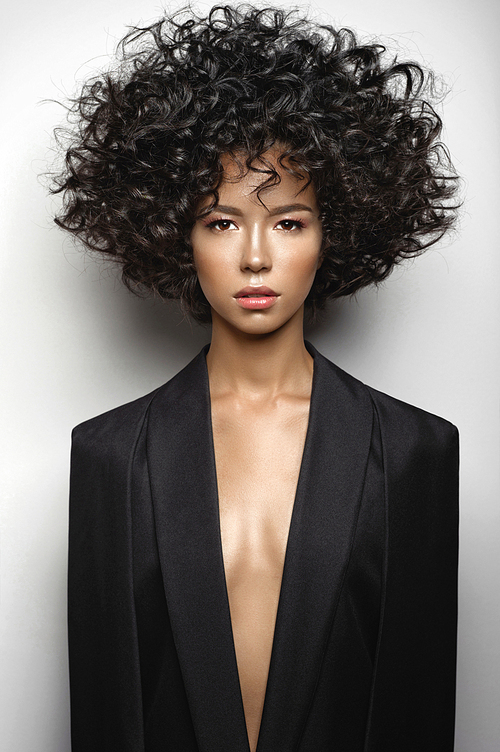 Fashion studio portrait of beautiful woman in black cape with afro curls hairstyle. Fashion and beauty