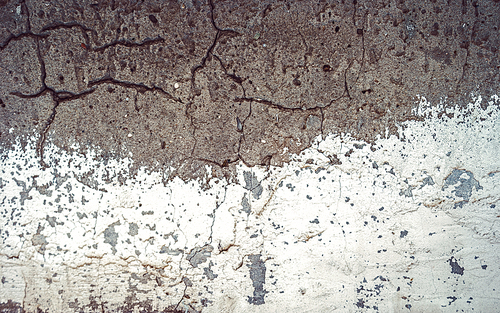 White and gray texture, cracked concrete wall, half painted with obsolete white paint.