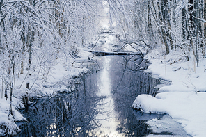 Small water channel in dreamlike snowy forest by winter morning