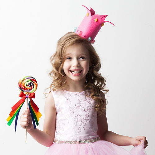 Beautiful little candy princess girl in crown holding big lollipop and smiling