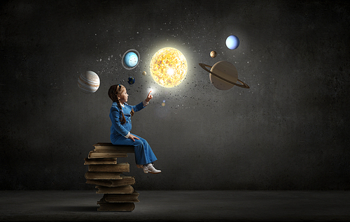 Little girl sitting on stack of books and touching planet