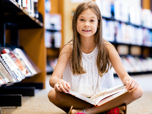 Little girl sitting on the floor and reading books in library