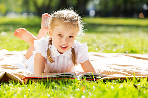 Little cute girl in summer park reading book