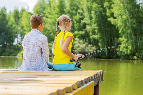 Rear view of two children sitting at bank and fishing