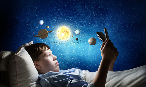 Teenage boy in pajamas lying in bed using tablet pc