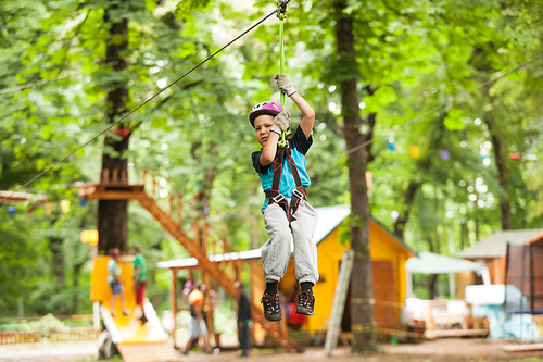 A boy in a helmet and safety equipment in adventure ropes park on the background of nature