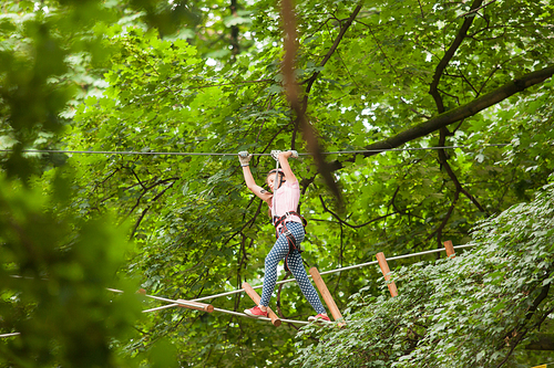 Teenage girl in a helmet and safety equipment in adventure ropes park on the background of nature
