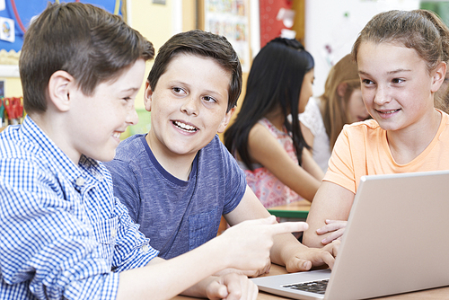 Group Of Elementary School Children Working Together In Computer Class