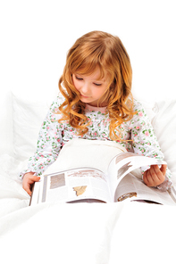 Cute little girl reading before sleep in her bed with white linen