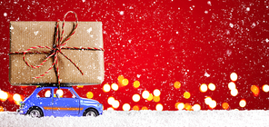 Blue retro toy car delivering Christmas or New Year gifts on festive red background