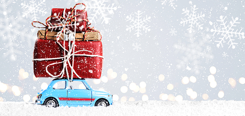 Blue retro toy car delivering Christmas or New Year gifts on festive gray background