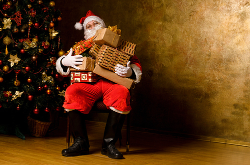 Tired Santa Claus sitting with gift boxes near decorated fir tree