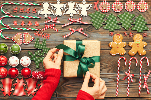 Female hands over christmas gift and homemade gingerbread cookie with handmade decoration on wooden background