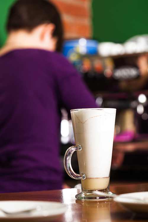 Barista is pouring milk in to a glass with caramel - preparing sweet and spicy coffee latte