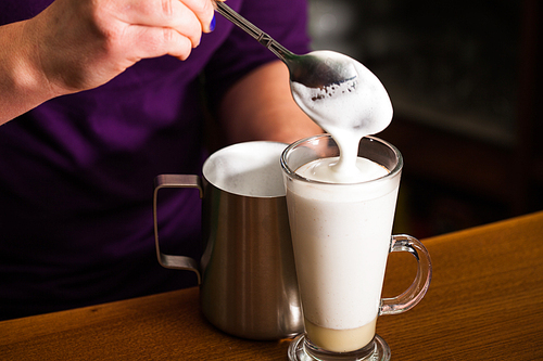 Barista is pouring milk foam in to a glass with caramel - preparing sweet and spicy coffee latte