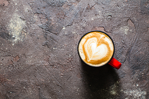 Latte art heart shape in the cup of cappuccino. Top view, vintage red cup on brown concrete textured background