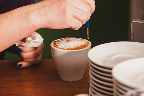 Barista making a cup of latte art coffee with special metal device - latte-art pen tool