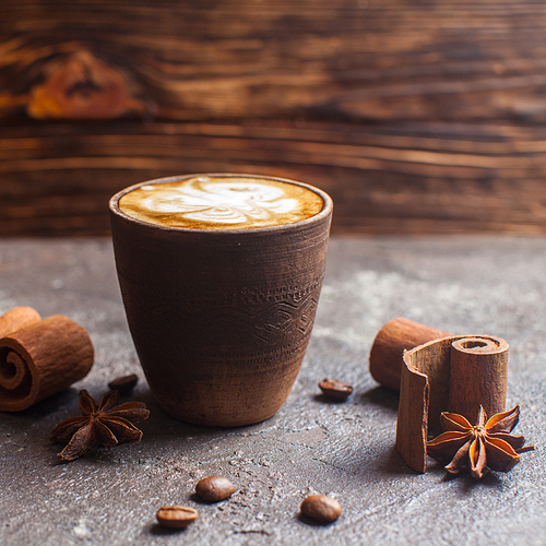 Capuccino in handmade clay cup with cinnamon and anise spices