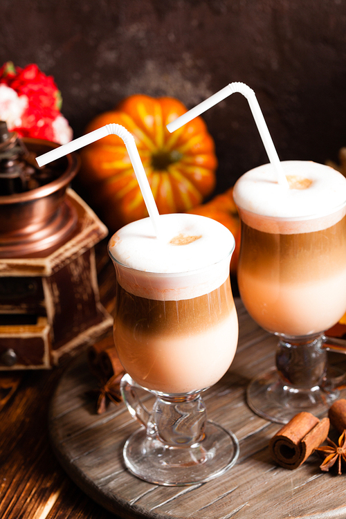 Two glasses pumpkin spicy latte with whipped cream and cinnamon on a wooden stand