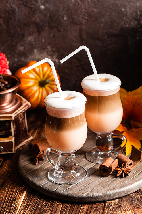 Two glasses pumpkin spicy latte with whipped cream and cinnamon on a wooden stand