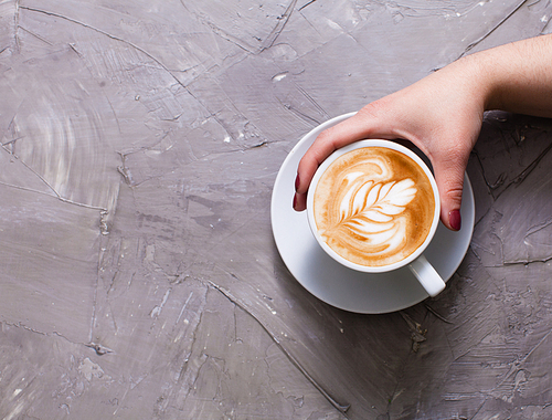Female hand holding a cup of cappuccino with figure cream. Top view with copy space